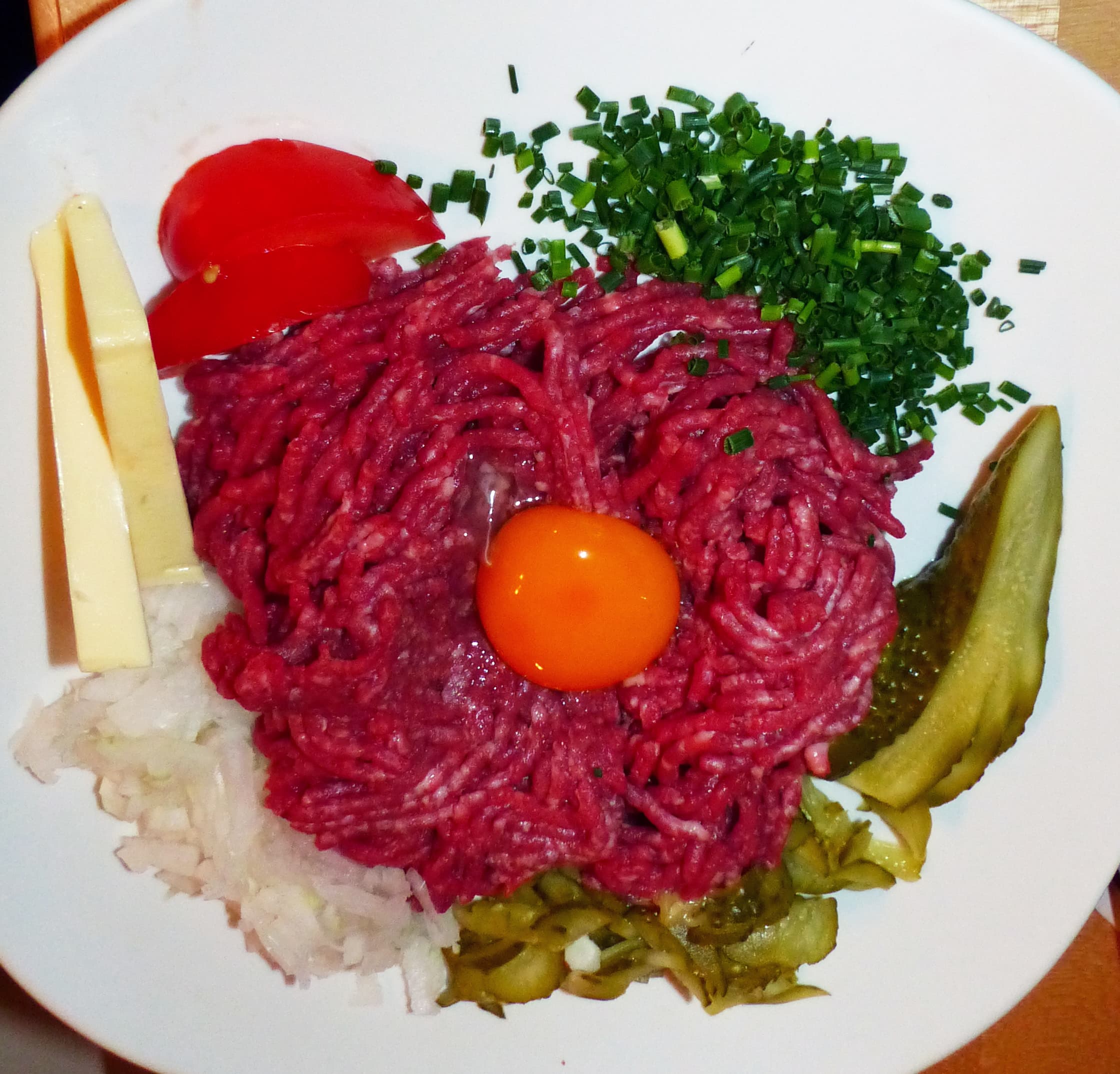 Steak tartare — a french main course dish from France — featuring raw beef, self-seasoned, egg yolk topped